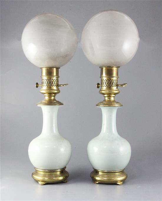 A pair of mid 19th century French ormolu mounted celadon porcelain oil lamps, with opaque circular glass shades, height 23in.
